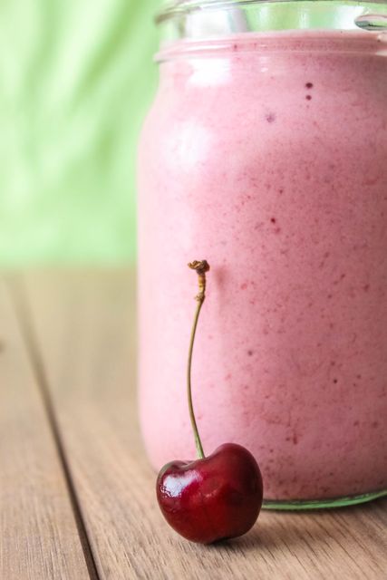 One cherry in front of glass jar with smoothie